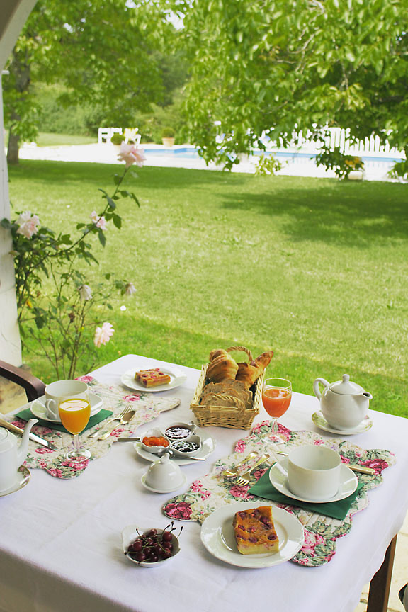 Table du petit-déjeuner avec ses confitures , cerises du jardin ,clafoutis "maison" ,jus de fruit, viennoiseries , pain de campagne avec vue sur le parc et la piscine.